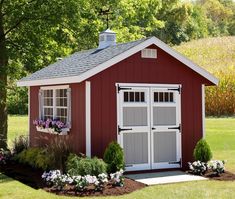 a red shed with white windows and flowers in the front yard, surrounded by trees