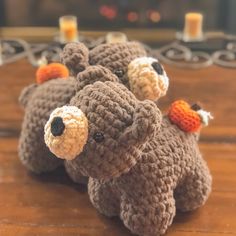 three crocheted teddy bears sitting on top of a wooden table next to candles