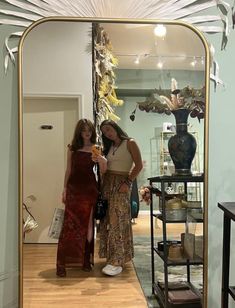 two women standing in front of a large mirror