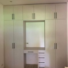 an empty room with white cupboards and drawers on the wall next to a bed