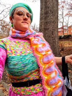 a woman in a colorful sweater and scarf holding a cell phone while standing next to a tree