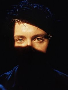 a man with long hair and blue eyes stares into the camera while wearing a black hat