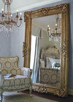 an ornate gold framed mirror sitting on top of a wooden floor next to a chair