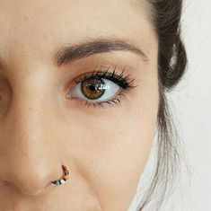 a close up of a person with piercings on her nose and eyeliner,