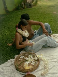 a man and woman sitting on the grass with flowers in front of their faces,