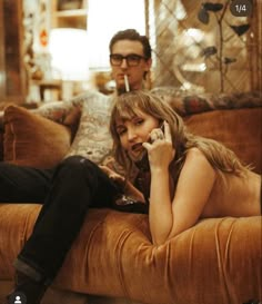 a woman sitting on top of a couch talking on a cell phone next to a man