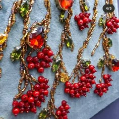 red berries and green leaves are attached to gold - plated necklaces on a piece of fabric