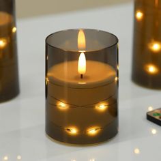 a lit candle sitting on top of a table next to two remotes and a cell phone