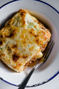 a white plate topped with lasagna covered in cheese and sauce next to a fork