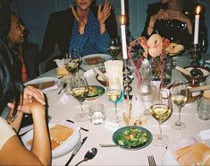 a group of people sitting around a dinner table with wine glasses and plates on it