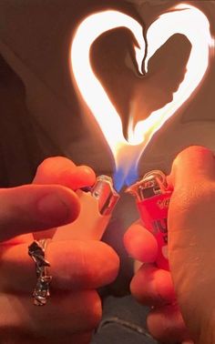 two hands holding lighters in front of a heart shaped light