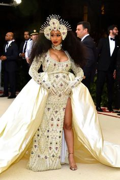 a woman in a white gown with an elaborate headpiece and long skirt, standing on the red carpet