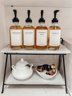 three bottles of liquid sit on a shelf next to a teapot and bowl with cloves