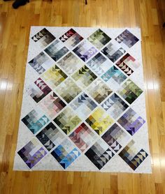 a quilt is laying on the floor in front of a wooden floor with a black cat standing next to it