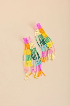 two pairs of multi - colored tasseled earrings on a white surface, one with yellow and pink fringes