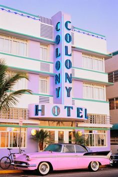 an old pink car parked in front of a tall building with the word colony hotel on it's side