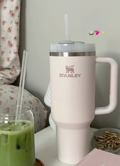 a pink coffee cup sitting on top of a table next to a green smoothie