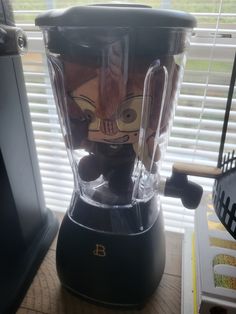 a blender sitting on top of a wooden table next to a window with blinds