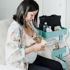 a pregnant woman sitting on a couch looking at her cell phone while holding something in her hand