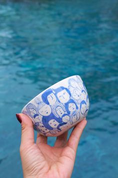 a hand holding up a blue and white bowl in front of a body of water