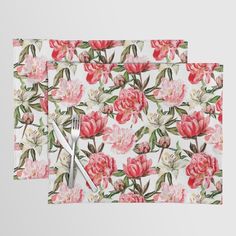 two placemats with pink flowers and green leaves on them, one has a fork in the middle