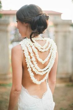 the back of a woman's wedding dress with flowers in her hair and necklace