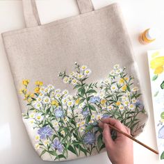 someone is painting flowers on a canvas bag