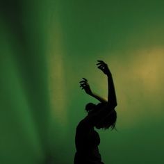 a woman standing in front of a green wall with her arms up and hands raised