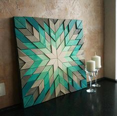 two candles are sitting on a table next to a wooden wall decoration with an abstract design