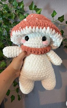 a hand is holding a crocheted stuffed animal with an orange and white hat