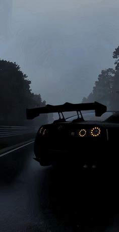 a black sports car driving down a wet road at night with trees in the background