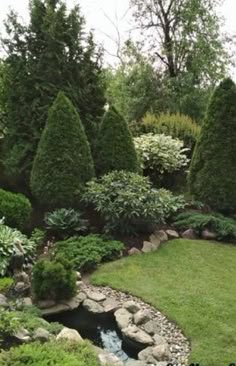 a garden with lots of green grass and trees around it, including rocks and water