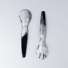 two spoons that are sitting next to each other on a white surface with black paint