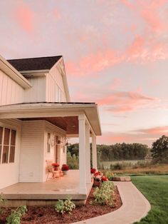 a white house sitting on top of a lush green field next to a forest at sunset