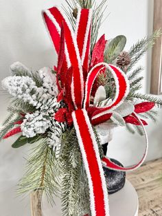 a red and white bow on top of a vase filled with evergreen, pine cones and candy canes