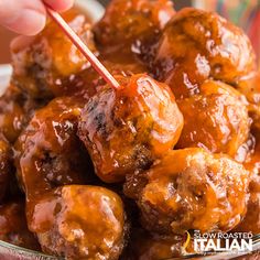 someone is holding a toothpick over some meatballs in a bowl with sauce