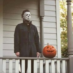 a man standing on a porch with a jack o'lantern in front of him