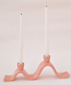 two candles are sitting on top of a pink candle holder that is shaped like a wave