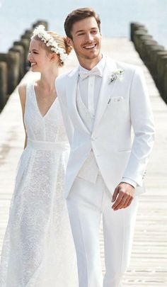 a bride and groom are walking on the pier at their wedding day, dressed in white