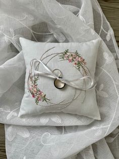 a white pillow with flowers on it and a ring in the middle sitting on a bed