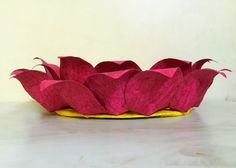 a pink flower sitting on top of a yellow plate next to a white wall in the background