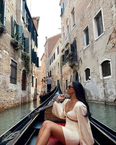 a woman sitting on the back of a boat in a narrow canal next to buildings