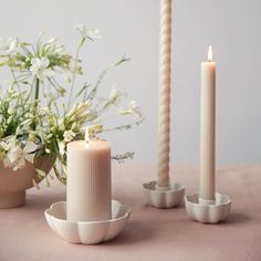 two white candles sitting on top of a table next to some vases and flowers