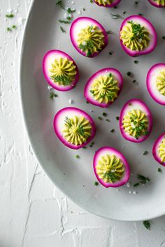 small deviled eggs with yellow and pink decorations on a white plate, garnished with parsley