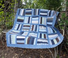 a blue and white quilt sitting on top of a wooden bench in front of trees