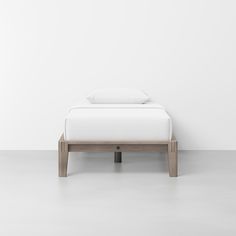 a white bed sitting on top of a wooden foot board next to a white wall