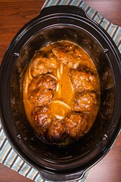 a crock pot filled with meat and gravy on top of a wooden table