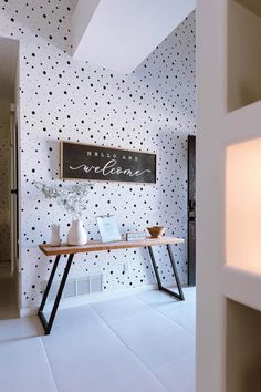 a room with black and white polka dot wallpaper, a wooden table topped with vases