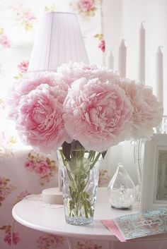 pink carnations in a glass vase on a small table next to a lamp