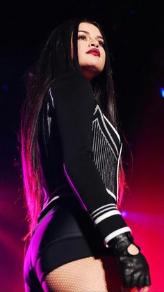 a woman with long black hair and gloves on her arm, standing in front of a stage